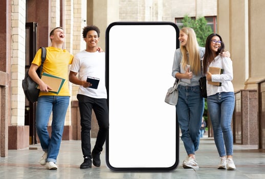 A group of four students enjoys a lighthearted moment outside a university building, passing by huge phone with blank screen photo