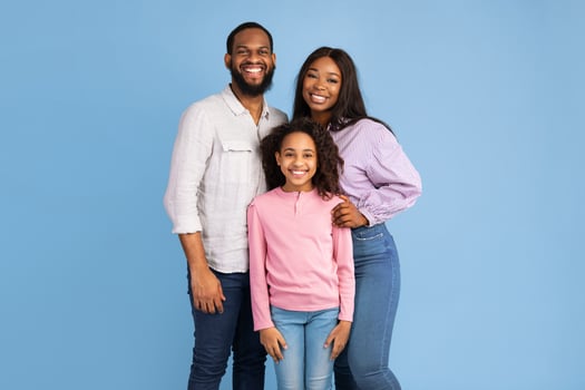 Happy Loving Family. Portrait of African American man, woman and girl standing isolated on blue studio wall. Smiling husband and wife posing with daughter looking at camera. Togetherness And Bonding photo