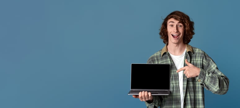 Excited millennial guy pointing at laptop computer with empty screen on turquoise background, space for your ad photo