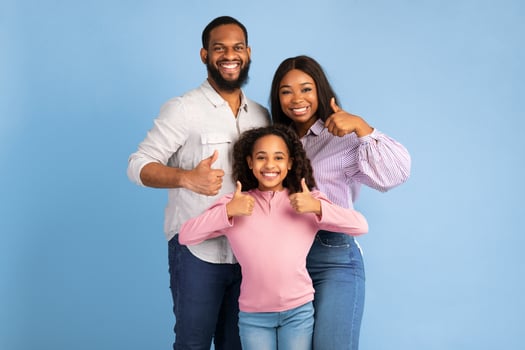 Best Choice, We Like It. Portrait of smiling black family showing thumbs up gesture with both hands, approving or recommending something good. Mom, dad and daughter standing isolated on blue wall photo