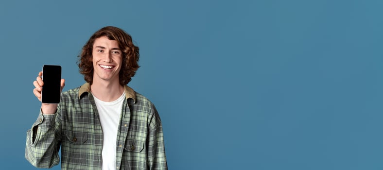 Happy Caucasian teenager showing mobile phone with blank screen on color background, space for your design photo