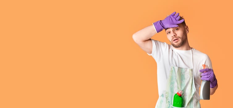 House cleaning concept. Tired man in apron and gloves wipes his forehead photo