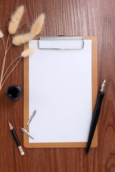 Blank clipboard with dip pen and dried grass on wooden texture background. photo