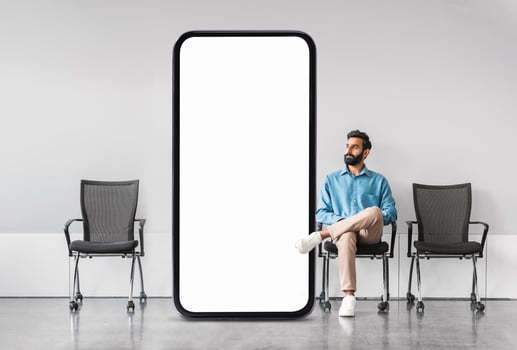 Arab man casually sits next to a large blank screen in a contemporary waiting area, creating an intriguing contrast in space and emphasizing the minimalist design of the environment. photo