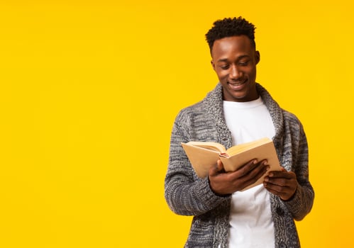 Romantic african guy reading poetry in old book on yellow background, copy space photo