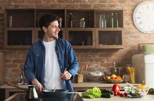 Happy man cooking delicious and healthy food in the loft kitchen at home on sunny day. Preparing vegetable salad. photo
