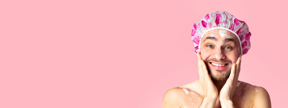 Morning shower. Funny guy washing his face and smiling on pink background photo