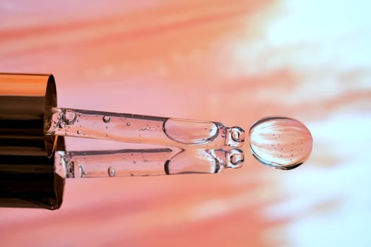 A pipette with facial serum against a sunset background in bright orange tones. photo