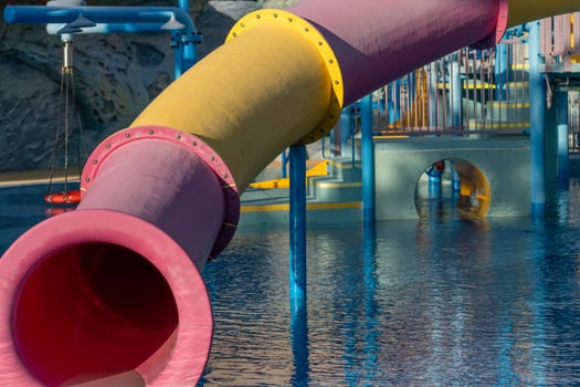 Waterpark Slide Pool Fun - Close-up of a pink and yellow water slide at a waterpark. The slide is situated above a blue pool. photo