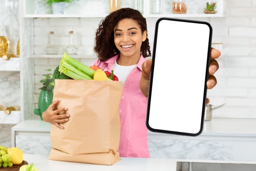 Food Delivery Service. Smiling black woman holding credit card and paper bag with food, standing in kitchen, free space photo