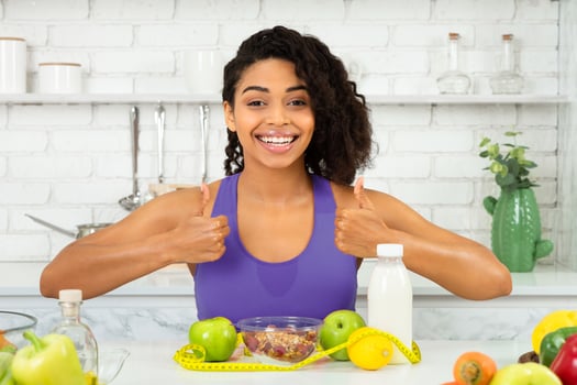 Successful Diet Concept. Excited slim african woman showing thumbs up, sitting with healthy breakfast in kitchen photo
