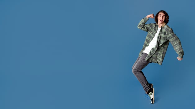 Cheerful young man standing on tiptoes against color background, blank space photo