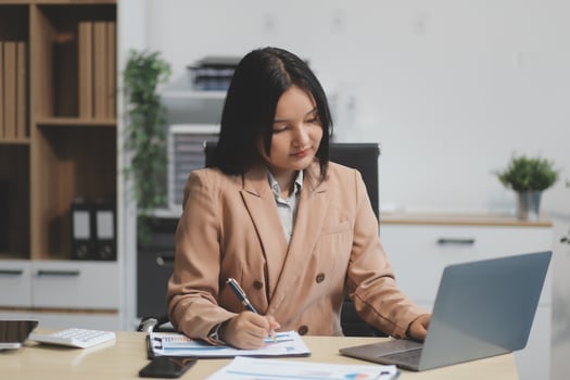 Asian Businesswoman Using laptop computer and working at office with calculator document on desk, doing planning analyzing the financial report, business plan investment, finance analysis concept. photo