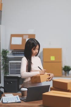 Startup SME small business entrepreneur of freelance Asian woman wearing apron using laptop and box to receive and review orders online to prepare to pack sell to customers, online sme business ideas. photo
