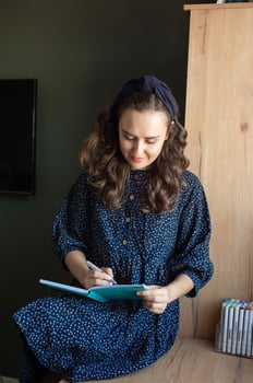 Smiling Woman in Blue Dress Writing in Notebook photo