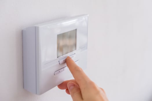 Hand adjusting digital thermostat on wall to control room temperature photo