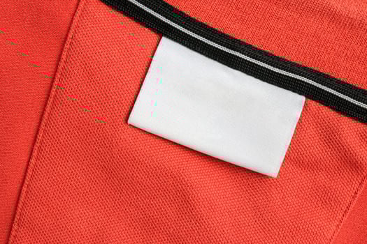 Blank white laundry care clothes label on orange shirt fabric texture background photo