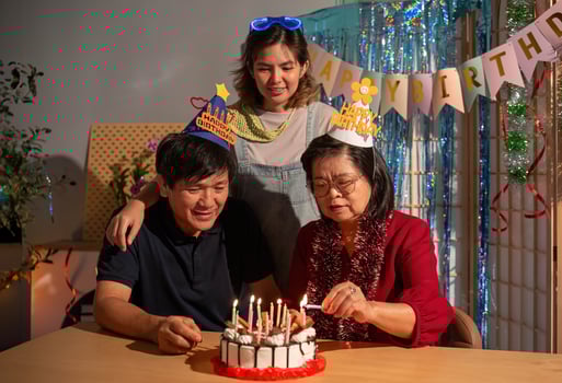 A woman is cutting a birthday cake with candles while two other people look on photo