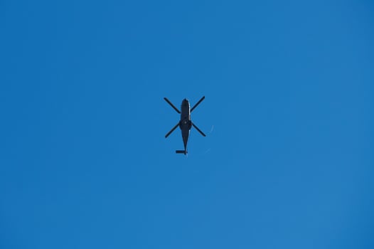 Silhouette of a helicopter flying against a clear blue sky photo