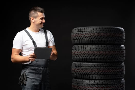 Mechanic holding tablet and looking at winter tires on black background photo