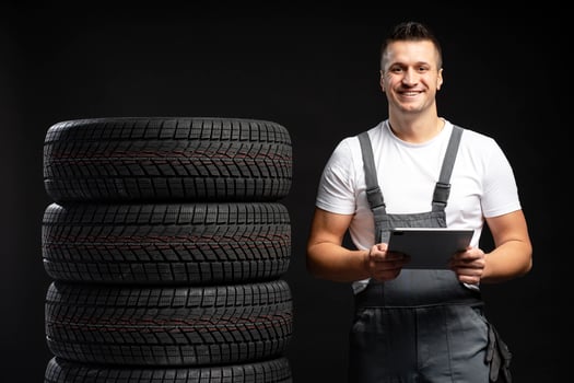 Mechanic holding tablet and smiling near stack of winter tires on black background photo