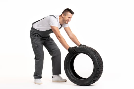 Mechanic pushing large tire on white background photo