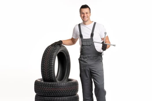 Mechanic holding lug wrench and leaning on stack of tires photo