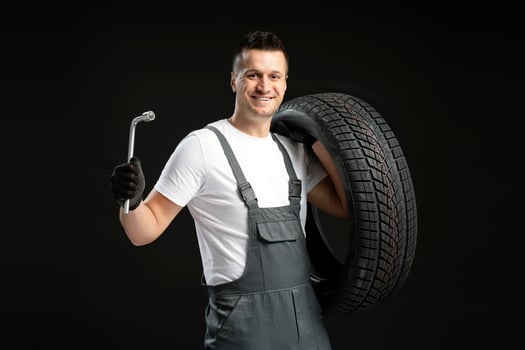 Mechanic holding lug wrench and tire smiling on black background photo