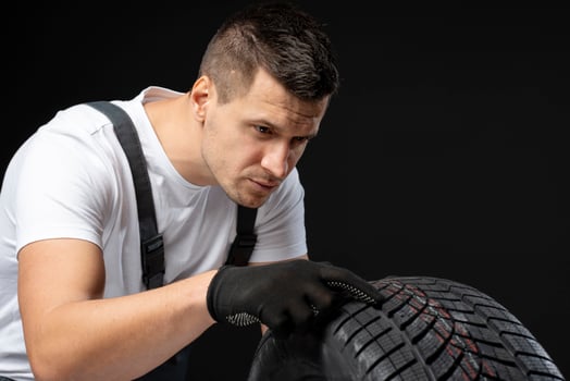 Mechanic inspecting winter car tire tread depth on black background photo