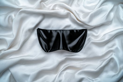 black satin eye mask on white silk sheets photo