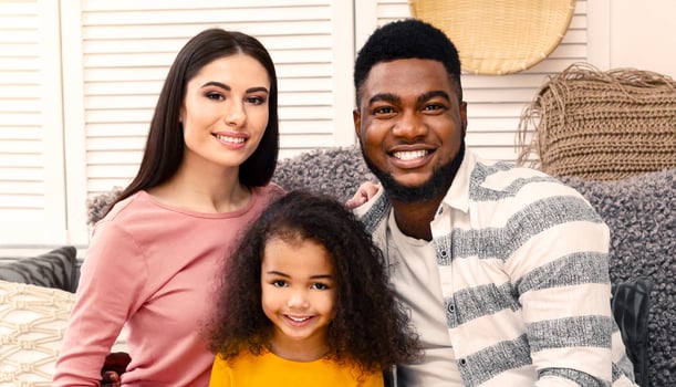 Smiling young international family with little daughter sitting on couch at home photo