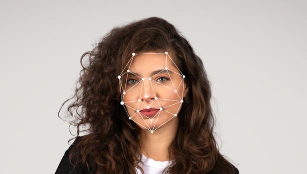 A woman stands against a plain background while facial recognition markers are displayed on her face. She has curly hair and a confident expression as the technology analyzes her features. photo