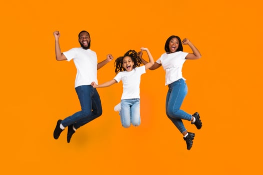 Yes. Full body length of excited young black family of three jumping and shaking clenched fists. Happy African American man, woman and girl celebrating victory together on yellow studio background photo
