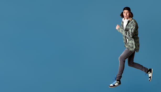 Funky millennial guy with headphones jumping on turquoise background, copy space photo