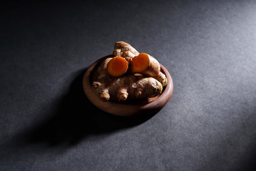 Fresh turmeric root and slices in wooden bowl isolated on dark background, turmeric Curcuma longa Linn, spice concept photo