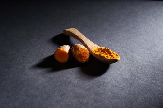Fresh turmeric root and turmeric powder in wooden spoon, turmeric isolated on dark background, spice concept photo