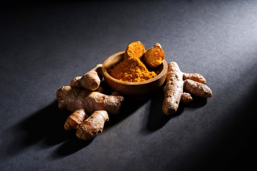 Fresh turmeric root and turmeric powder in wooden bowl, turmeric isolated on dark background, spice concept photo
