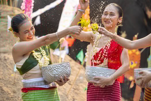Songkran festival. Northern Thai people in Traditional clothes dressing splashing water together in Songkran day cultural festival with sand pagoda and colorful paper flag. photo