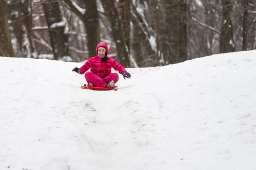 childhood, sledging and season concept - happy little girl sliding down on sled outdoors in winter photo