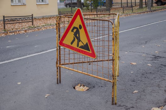 Road Repair sign. On the asphalt, the pit is fenced and there is a sign photo