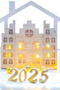 Golden figures number 2025 and tiny home on background of cozy windows of a house with warm light with festive decor of stars,snow and garlands. Greeting card, Happy New Year, cozy home photo