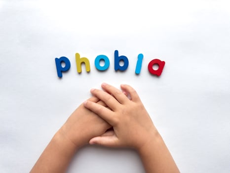 Childrens hands holding in anxiety concept with colorful phobia letters on white background photo