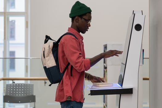 Young African student guy standing in library using self-service terminal to borrow or return books photo