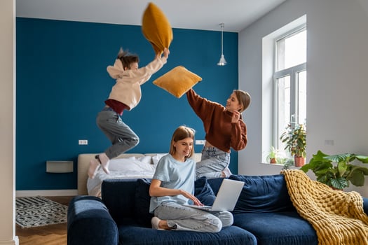 Naughty children fun playing pillow fight near busy smiling mother with laptop sitting on home sofa photo