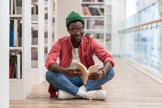 Happy African American millennial guy sitting on floor reading book while visiting library photo