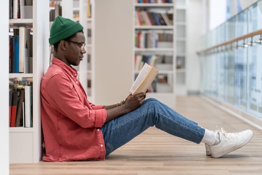 Concentrated African American student man with book spending free time in library, enjoying reading. photo