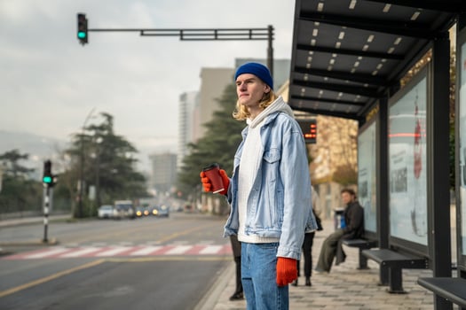 Young student guy waiting for bus. Man awaits at bus stop station. Public urban transport use photo
