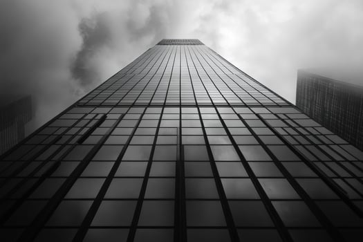 Modern glass skyscraper reaching into cloudy sky in black and white photo