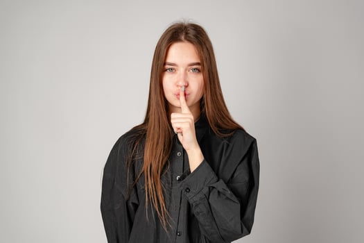 Smiling Young Woman Posing With Finger on Lips Against Grey Backdrop photo