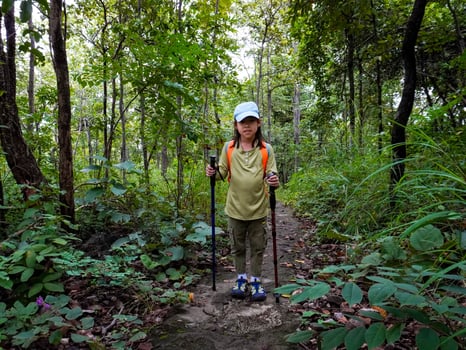 Asian girl hiking with backpack in rainy season and walking stick. photo